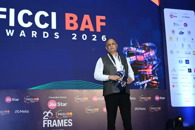 A winner stands with his FICCI BAF Awards 2026 trophy in front of the illuminated stage screen.