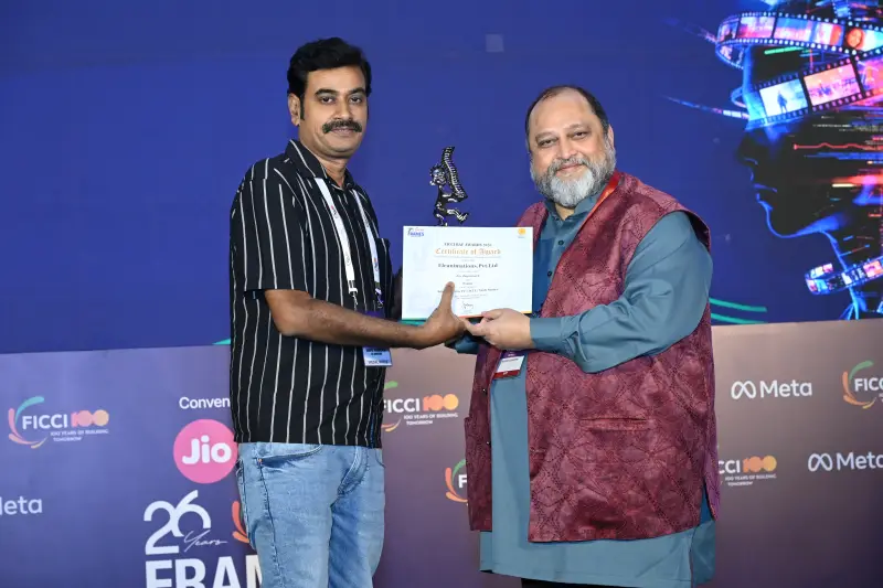 A winner in a striped shirt accepts his trophy and a handshake at the FICCI BAF Awards 2026.