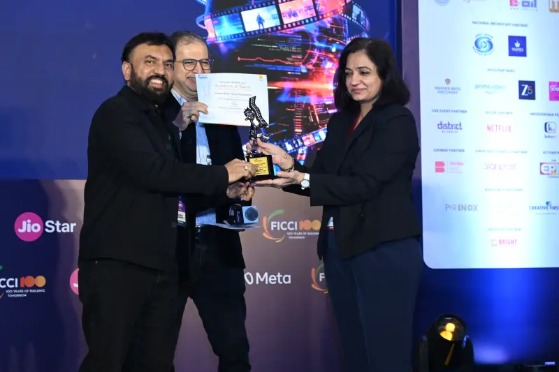 A winner receives his trophy and certificate from two presenters at the FICCI BAF Awards 2026.