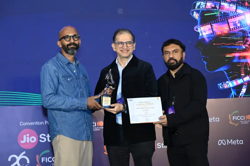 A winner holds his trophy and certificate between two presenters at the FICCI BAF Awards 2026.