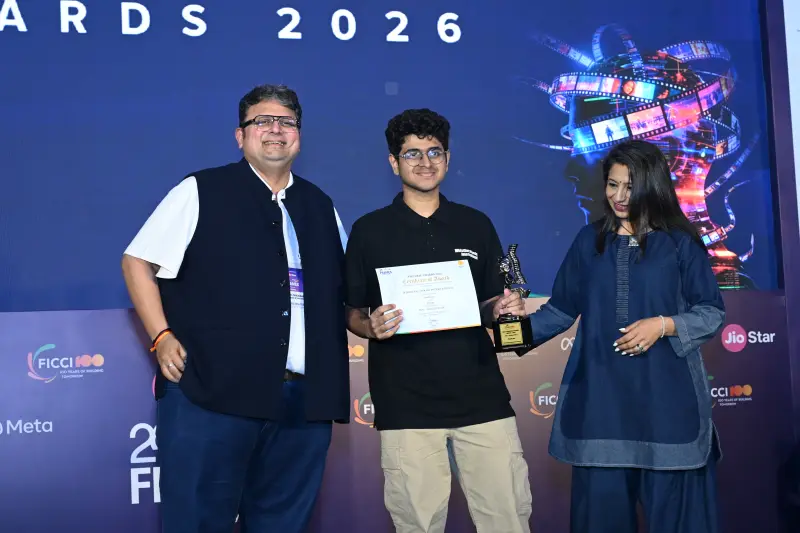 A young winner holds his certificate and trophy between two presenters at the FICCI BAF Awards 2026.