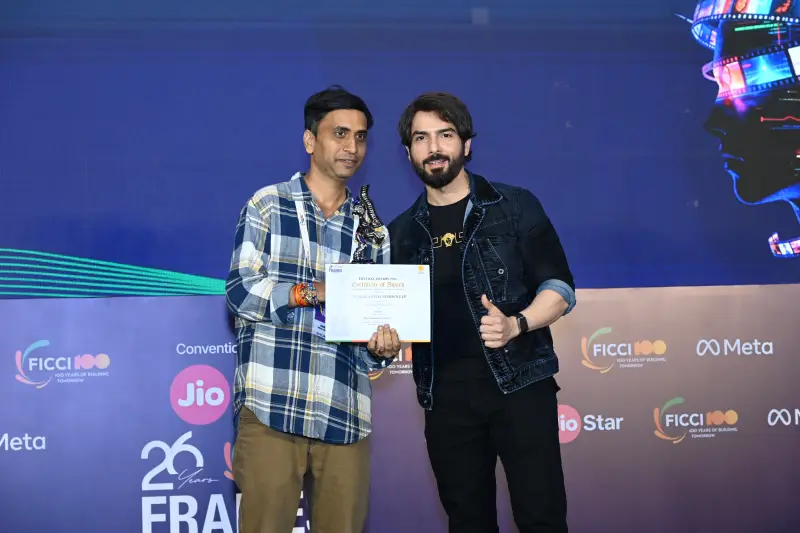 The host gives a thumbs-up beside a winner holding his certificate at the FICCI BAF Awards 2026.