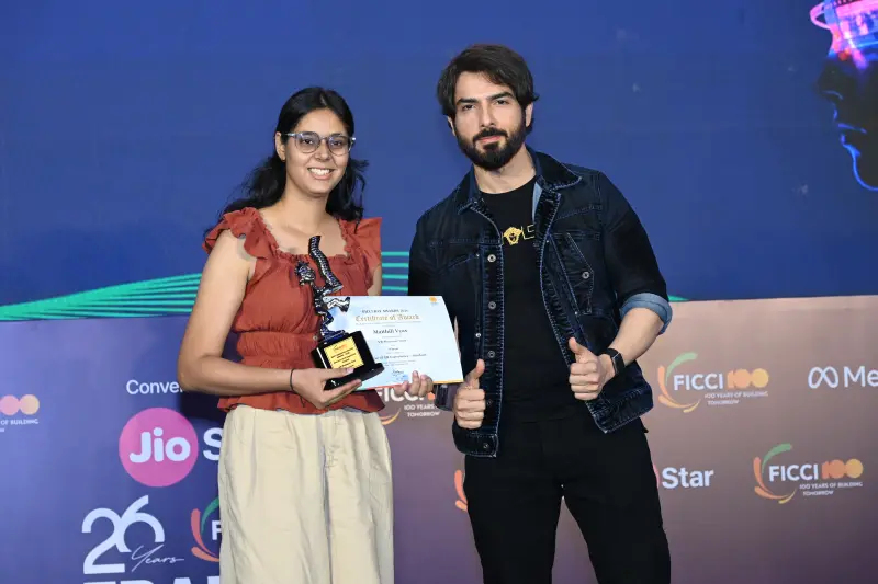 A winner holds her certificate and trophy beside the host at the FICCI BAF Awards 2026.