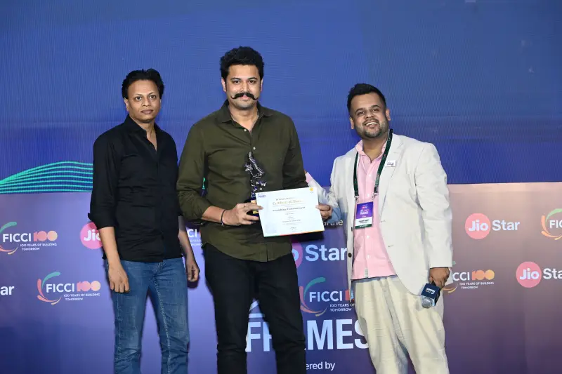 A winner holds his trophy and certificate between two presenters at the FICCI BAF Awards 2026.
